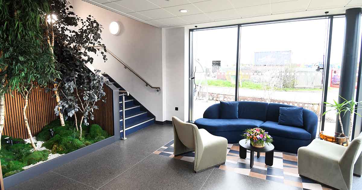 Freed Vaneers - Lounge area with blue sofa, plants, stairway, and large windows. 