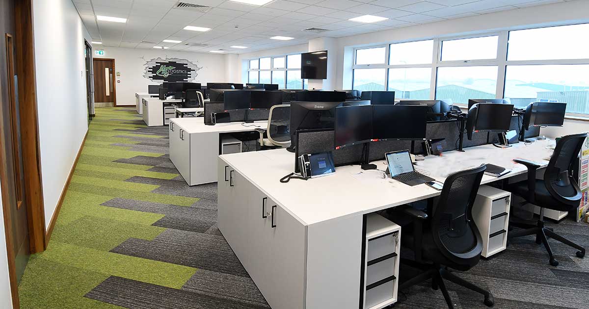  Modern office interior with desks, chairs, computers, and green carpet. - HBC