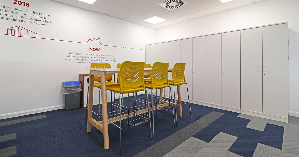 Office break area with yellow chairs, infographic wall, and storage cabinets.